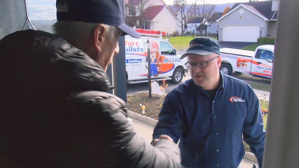 A technician greeting a man in a coat standing in his doorway.