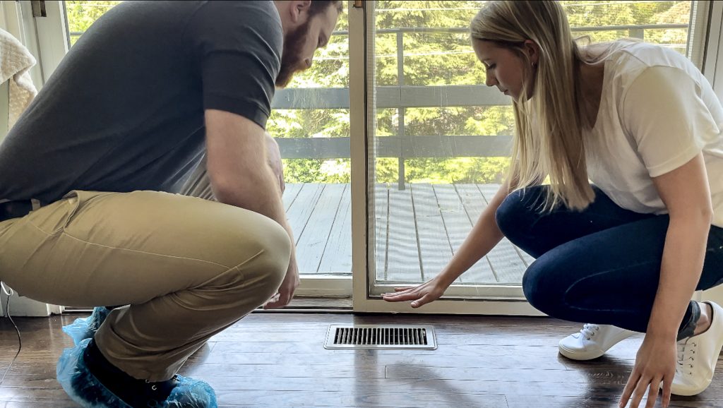 Two people feeling heat coming out of a vent