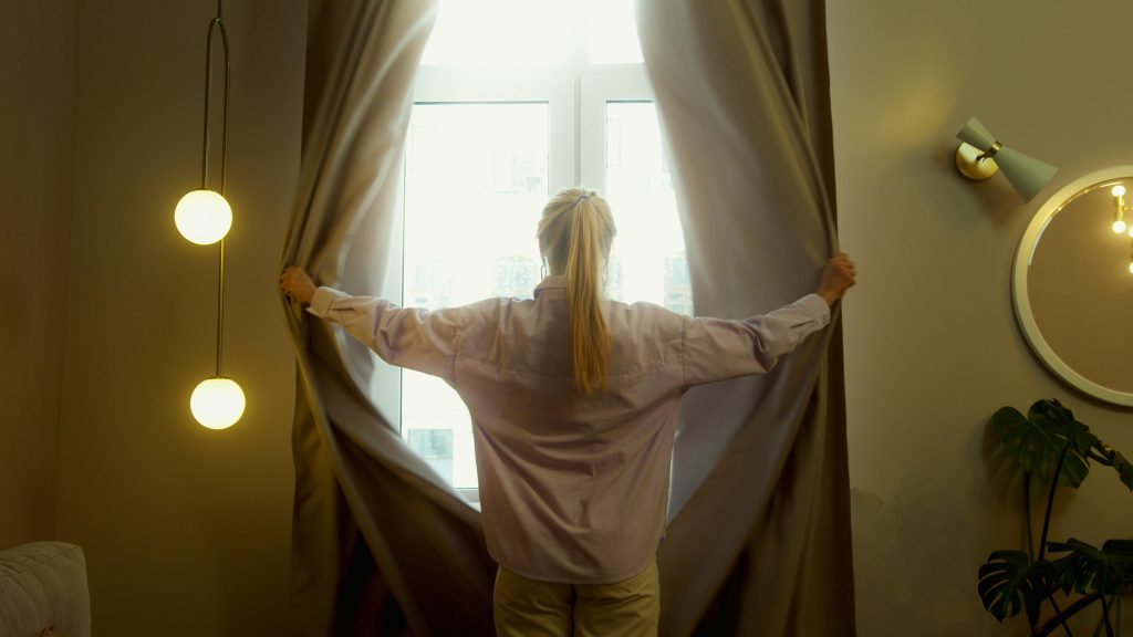 Woman drawing the curtains to let the sunshine in during early spring. 