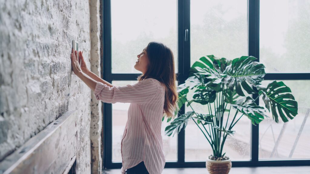 Lady looking at her thermostat on the wall.